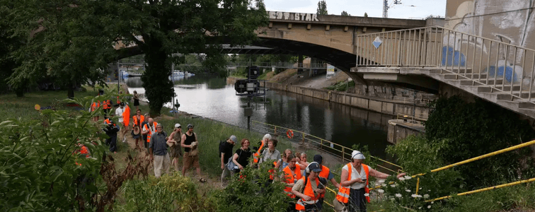 eilnehmende des Neckar Tribunals in Warnwesten steigen eine Treppe hinauf. Umgeben von Natur ist im Hintergrund der Neckar zu sehen, für dessen Schutz und Anerkennung als Ökosystem sich die Veranstaltung einsetzt.