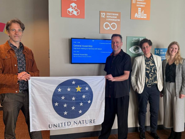 Delegierte aus Deutschland halten bei der UN-Versammlung „Harmony with Nature“ am Mother Earth Day 2025 die United-Nature-Fahne im UN-Gebäude in die Kamera.