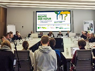 Teilnehmer*innen der Fachtagung „Rechte der Natur“ 2024 in den Räumen der FU Berlin, mit der Startseite der Präsentation im Hintergrund